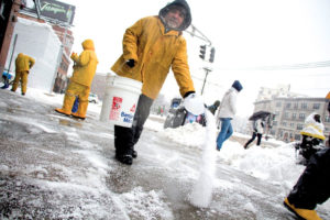 Man in yellow coat pouring salt on snowy road