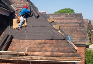 worker putting down tar paper during a roof replacement