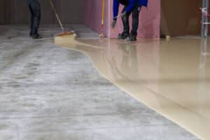 epoxy being poured on a concrete floor with two workers spreading it with tools